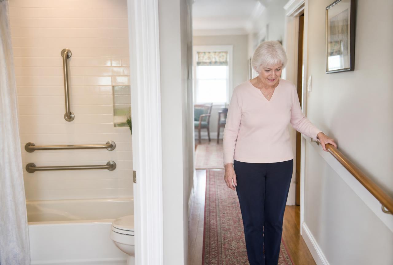 Preparing a Massachusetts Home for Aging in Place Older woman using a hallway handrail at home, with bathroom grab bars installed nearby